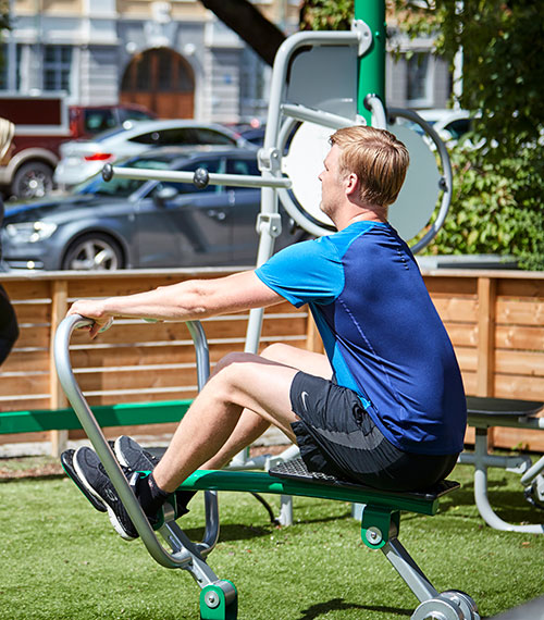 A man exercises on an outdoor gym machine at a residential setting.